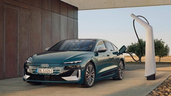 A teal electric Audi car is charging at a modern EV station in a contemporary outdoor setting.