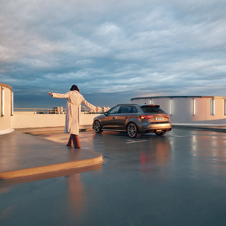 Kvinna balanserar över vattenpöl på parkering mot parkerad Audi