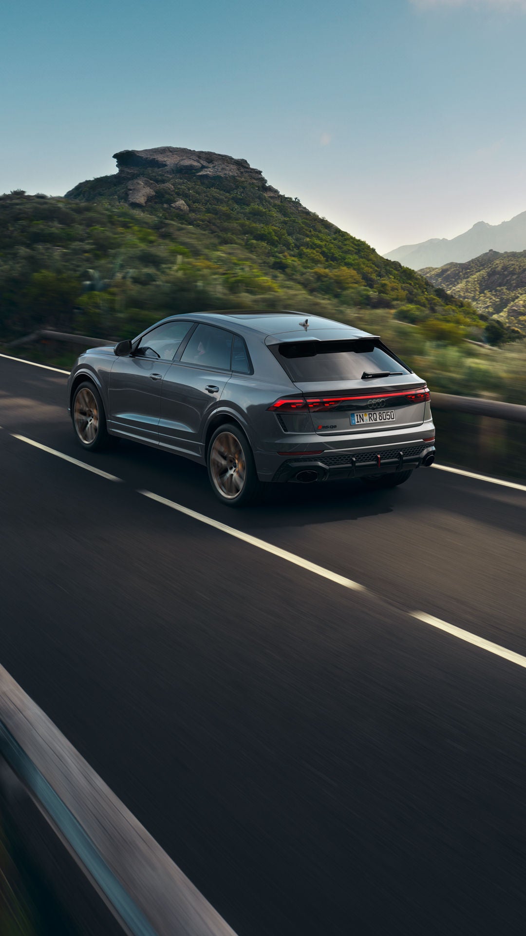 Der RS Q8 SUV schräg von hinten auf einer Gebirgsstraße. Im Hintergrund ragen bewaldete Wälder hervor.