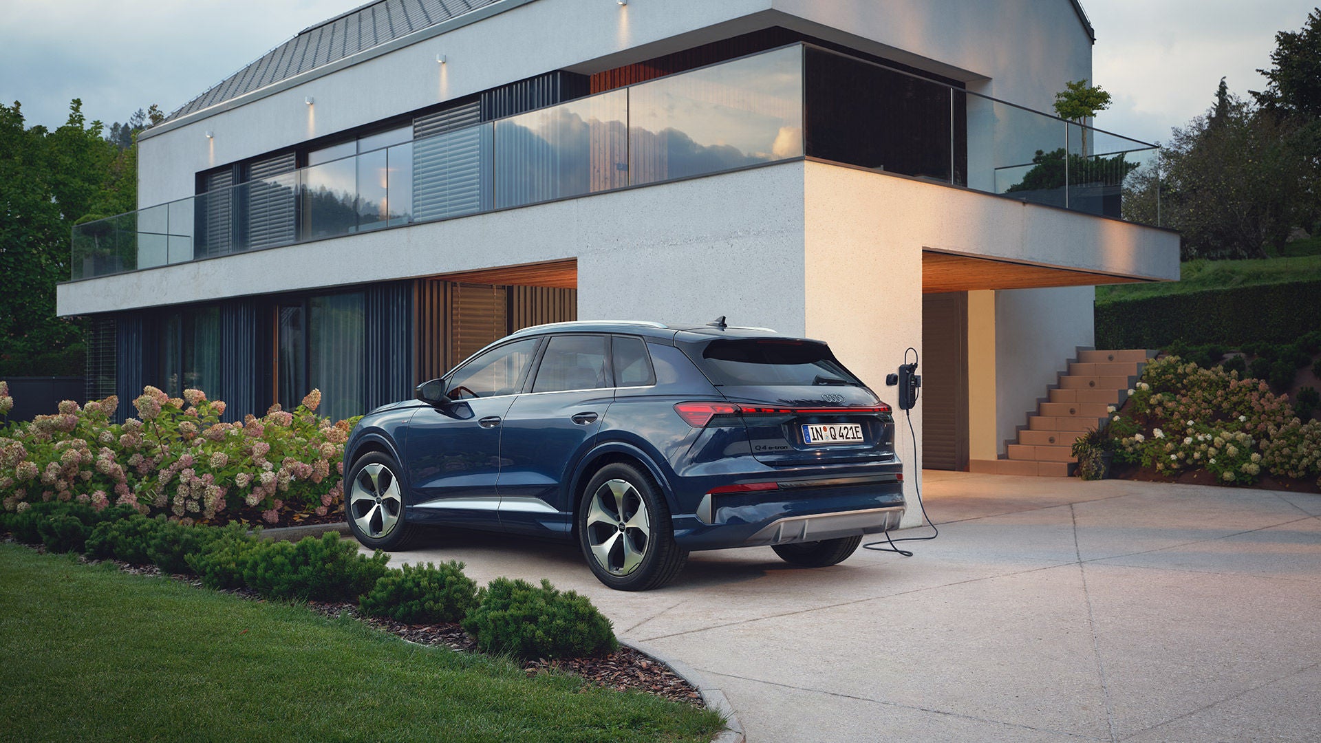 SUV électrique garé devant une maison avec borne de recharge.