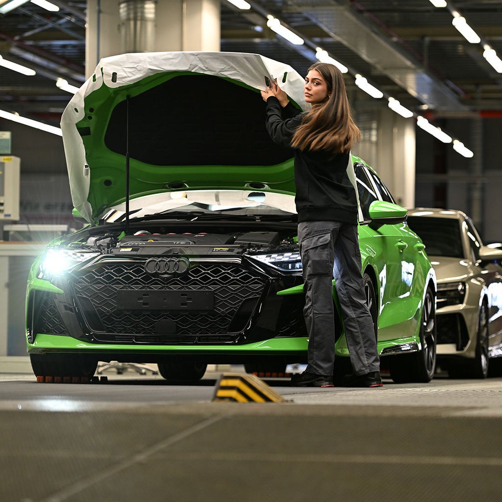 Emilia steht vor einer offenen Motorhaube eines grünen Audi