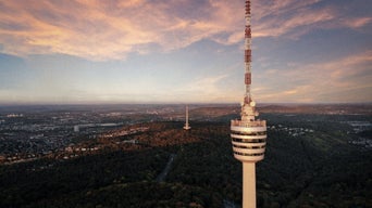 Stuttgarter Fernsehturm aus der Luft über bewaldeter Stadtlandschaft bei Sonnenuntergang.