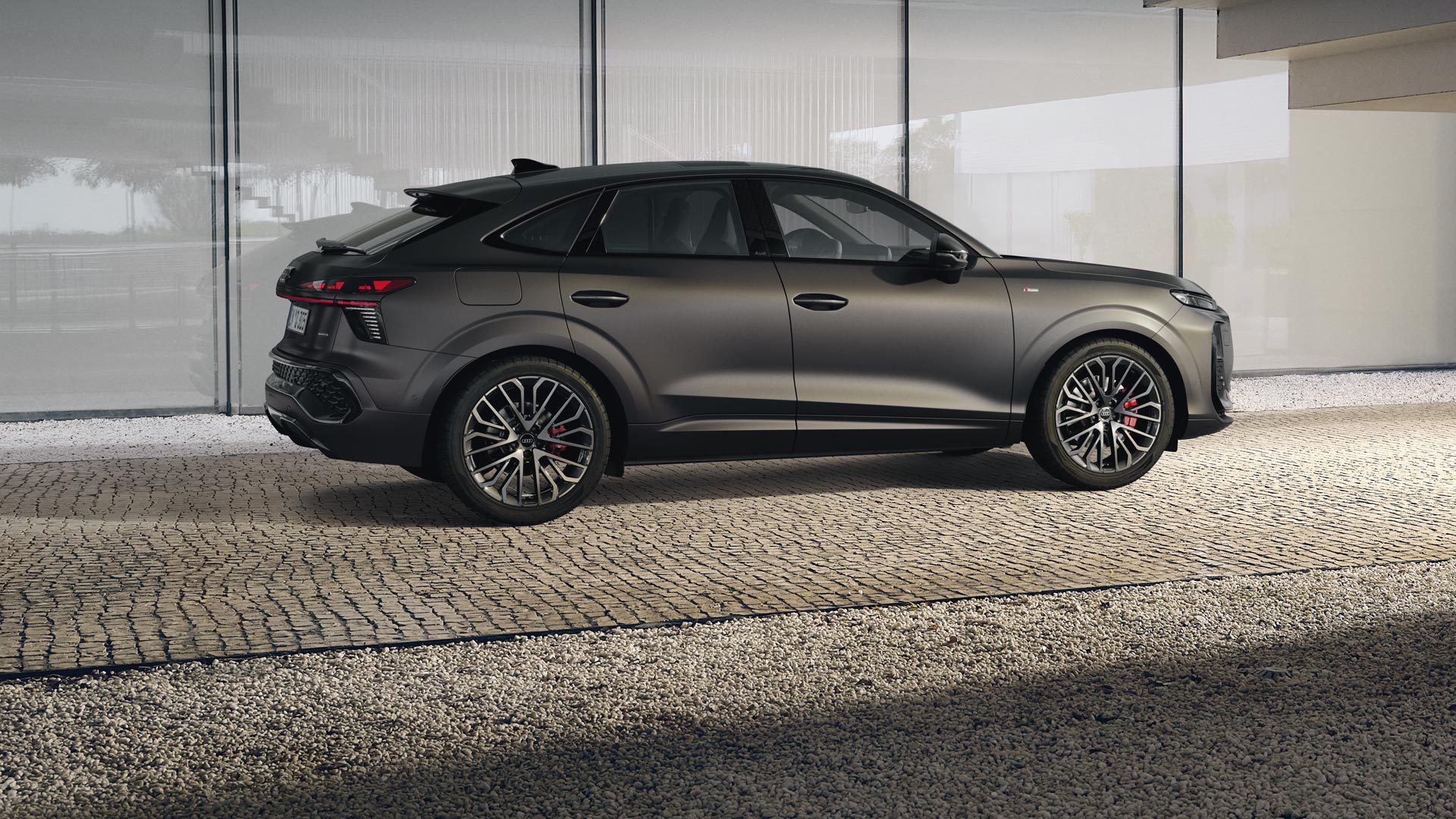 Vista posteriore del cockpit della Audi Q3 Sportback con volante, display panoramico e pacchetto di illuminazione ambientale rossa. Il mare è visibile attraverso il parabrezza.