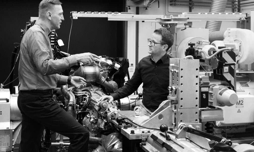 Dieter Weidemann und Bastian Heidler in der Diskussion an einem Antriebsstrang. Man erkennt Details eines Verbrennungsmotors und des Getriebes.