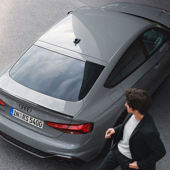Two people standing beside a parked grey Audi RS5 Sportback.