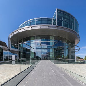 A modern round glass building with a ramp and a blue sky.