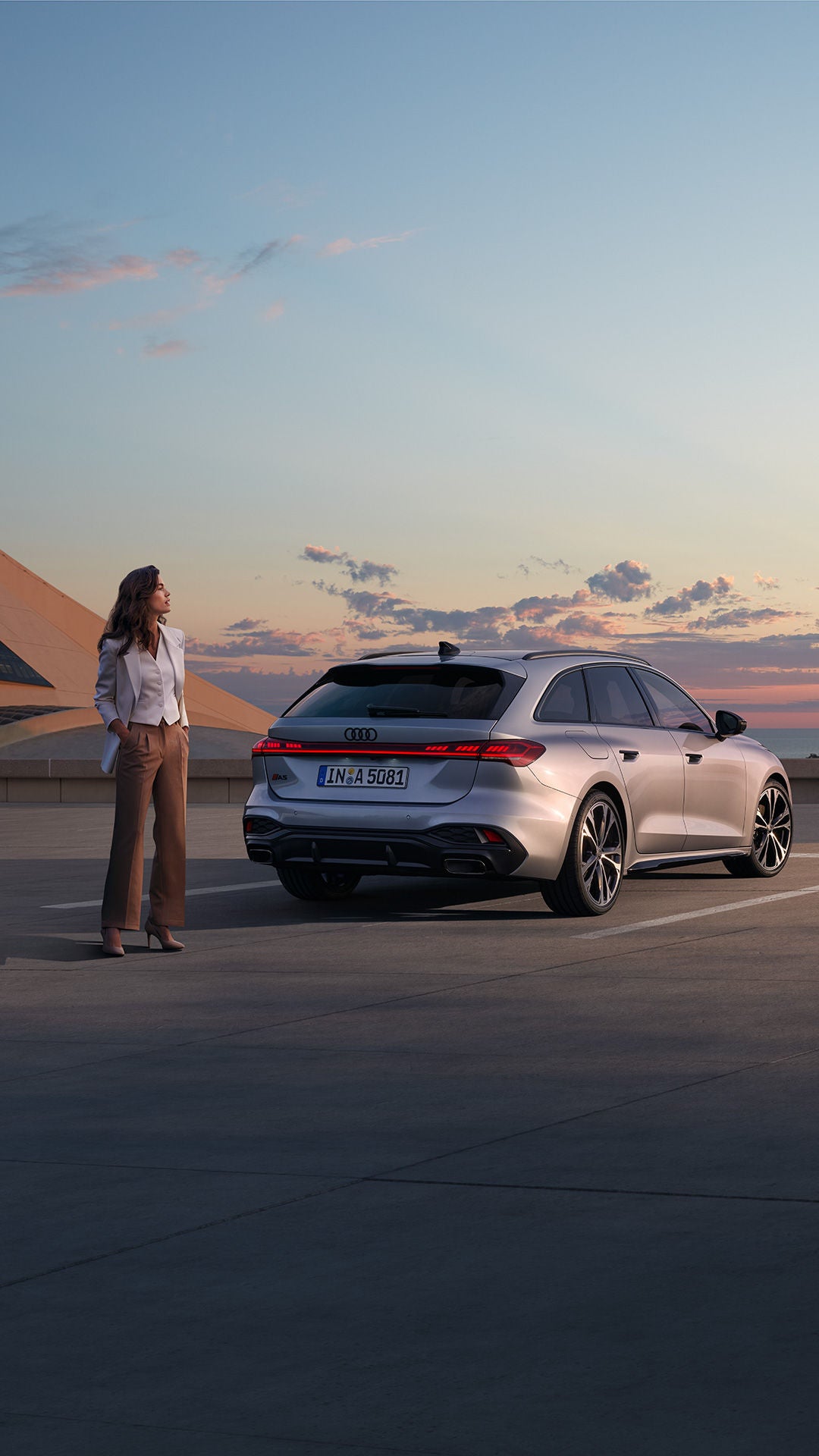 Frau im Businesslook steht neben einem silbernen Audi A5 Avant