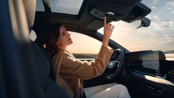 Fahrerin im Audi bedient Dachbedienfeld, Sonnenuntergang sichtbar durch Panoramadach.