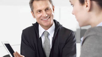 Berater im Anzug lächelt freundlich bei einem Gespräch mit Kundin und zeigt auf ein Tablet.