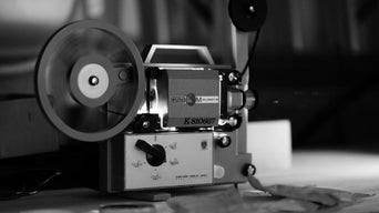 Schwarz-weiß-Foto eines alten Filmprojektors mit Filmrolle, auf einem Tisch stehend.