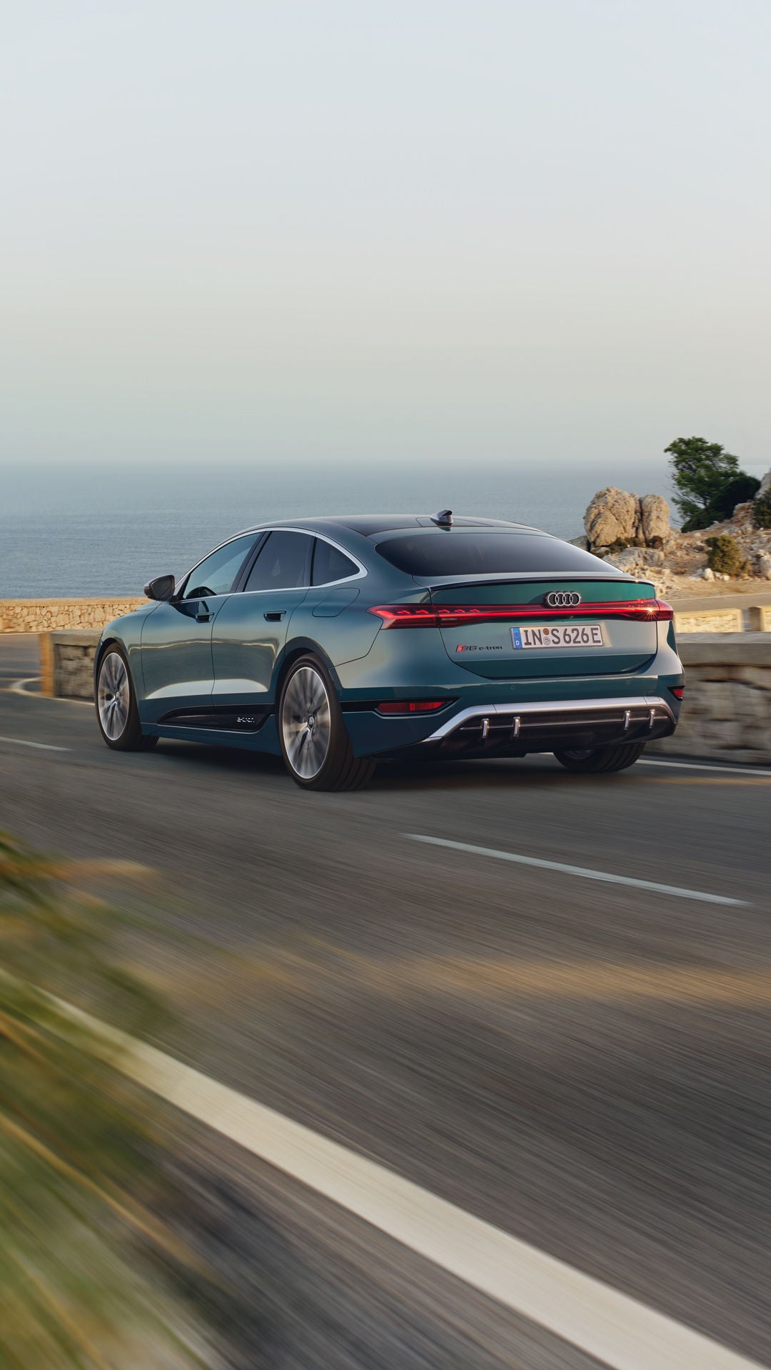 Der S6 Sportback e-tron im schrägen Heckprofil, während er eine kurvige Küstenstraße entlangfährt.