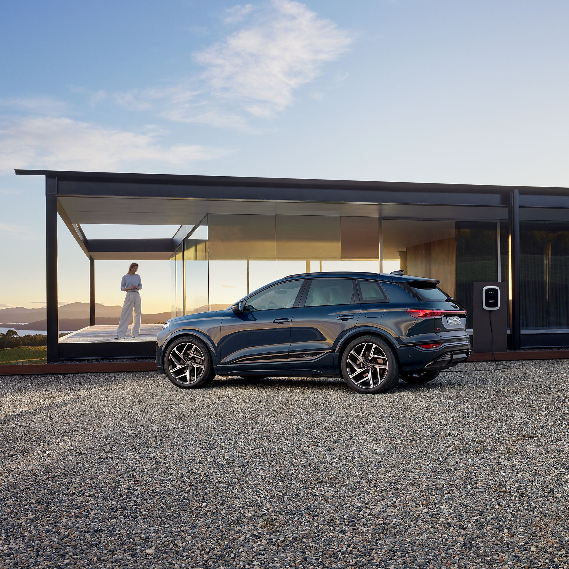 Audi Q6 e-tron står framför en byggnad, i bakgrunden står en person ute på en veranda
