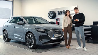 Zwei Personen stehen neben einem grauen Audi Q4 e-tron in einer Werkstatt und schauen gemeinsam auf ein Tablet.