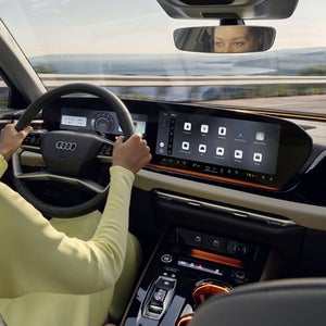 View from the back seat into the cockpit of the A5 Saloon. A woman is holding the steering wheel with both hands.