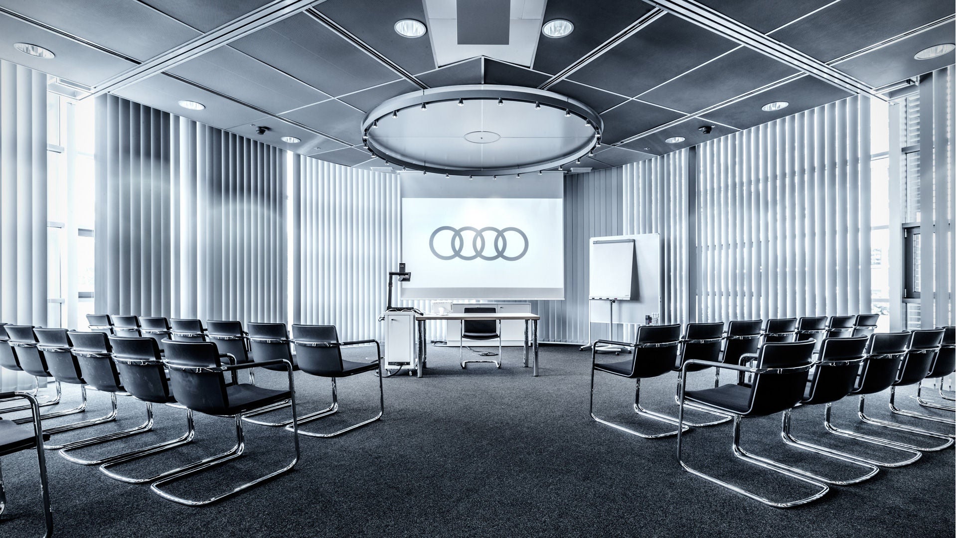 Modern conference room with empty rows of chairs and Audi logo on a screen.