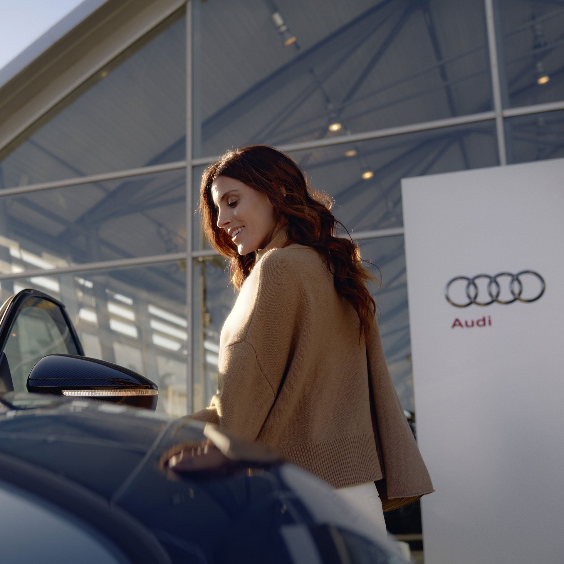 Eine Frau schaut runter auf die Autotür eines Audis, welches sie öffnet. Sie steht vor einem Audi Händler.