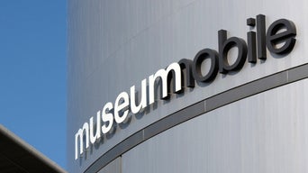 Schriftzug „museum mobile“ an der modernen Metallfassade eines Gebäudes vor blauem Himmel.