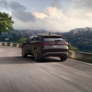 A Q3 Sportback drives along a curving mountain road. The background features misty mountains under a partly cloudy sky, evoking a sense of adventure.