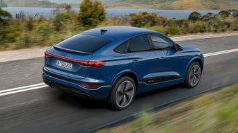 Schräge Heckaufnahme des SQ6 Sportback e-tron, welcher eine Straße an einem See in einer bergigen Landschaft entlangfährt.