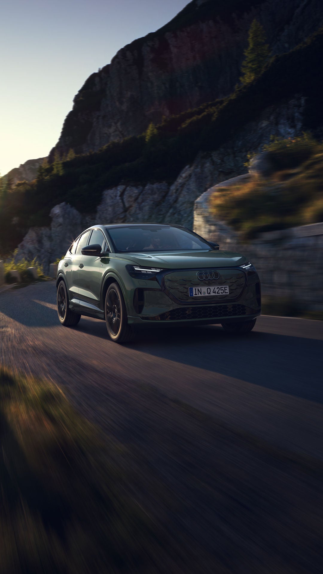 De Audi Q4 Sportback e-tron, ’s nachts van achteren gezien op een bochtige bergweg, met rechts de zee. Op de tegenliggende rijbaan zijn de koplampen van naderende voertuigen te zien.