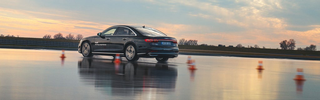 Schwarzer A8 50 TDI quattro auf nasser Strecke mit Parcour, im Hintergrund ist die Abenddämmerung.
