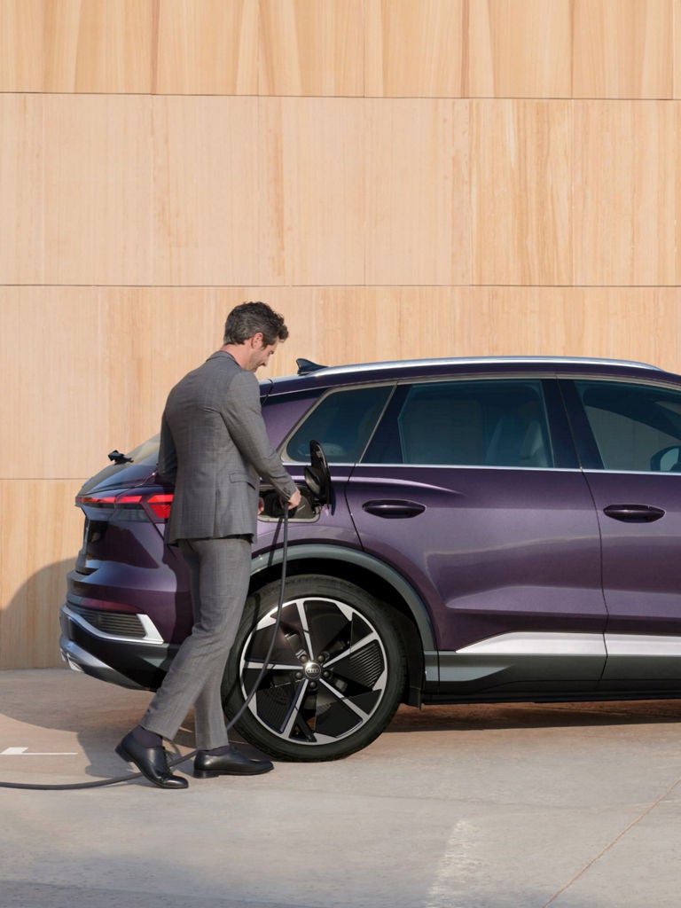 A person charging a purple electric SUV parked beside a wooden wall.