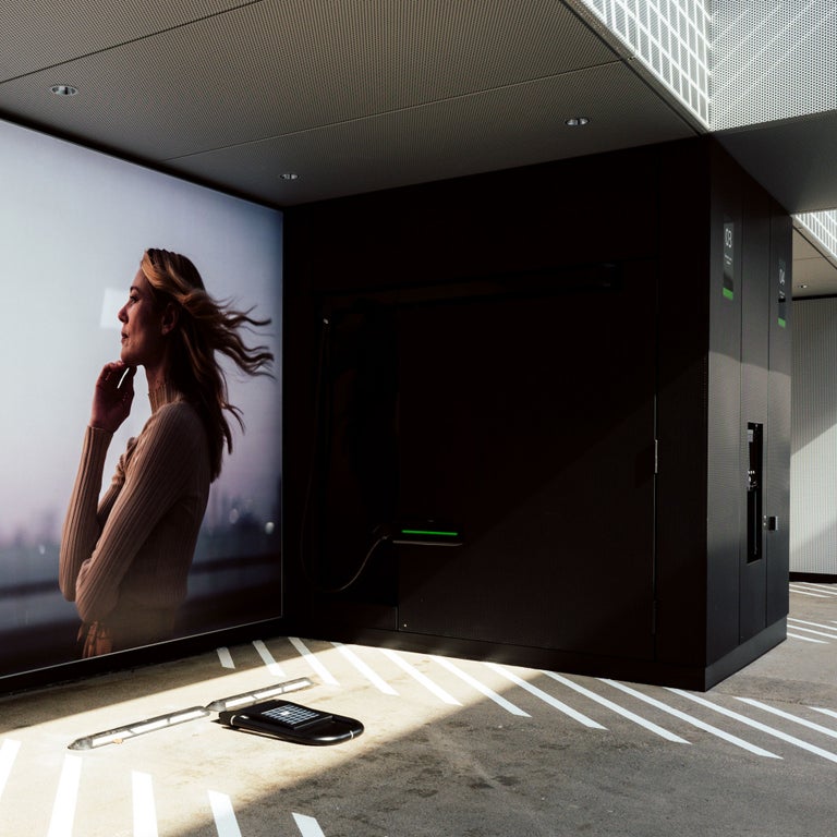 Ladestation mit großem Wandbild einer Frau im Wind und Bodenladeeinheit ohne Fahrzeug, daneben ein Infodisplay.
