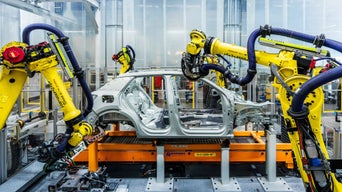 Robot arms assemble an unpainted car body in a production hall.