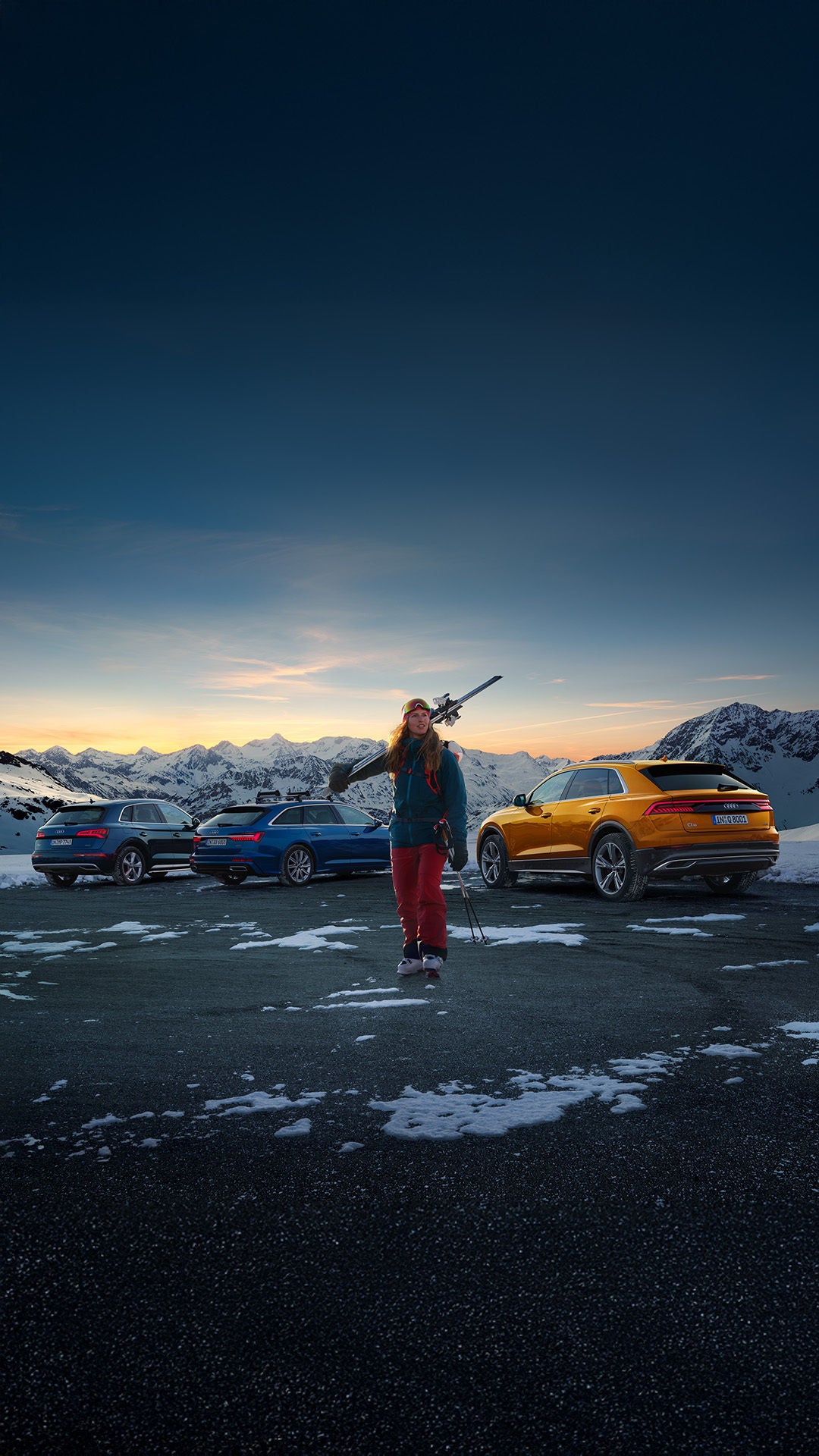 Eine Skifahrerin läuft vor drei Audi Fahrzeugen in den Bergen bei Sonnenuntergang.