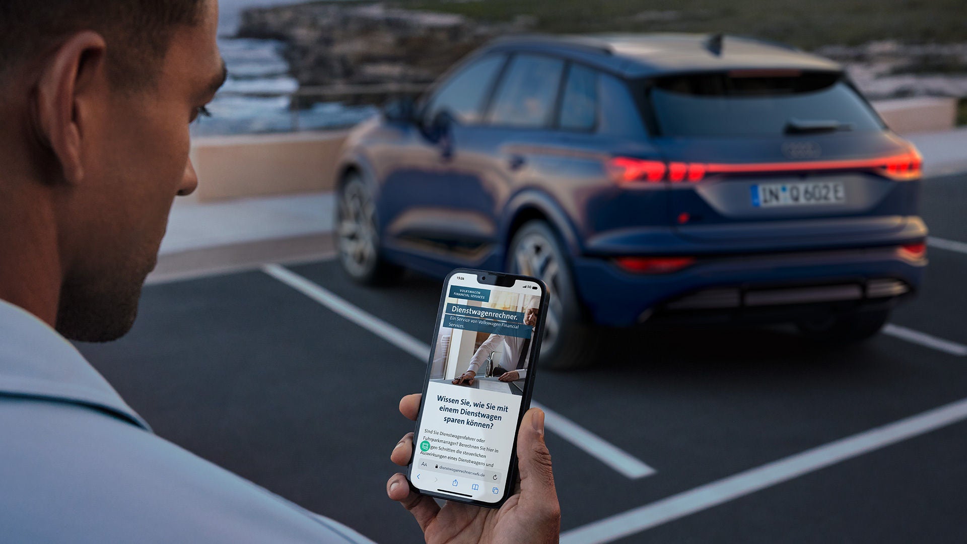 Mann schaut auf Smartphone, im Hintergrund steht ein Audi SUV auf einem Parkplatz.