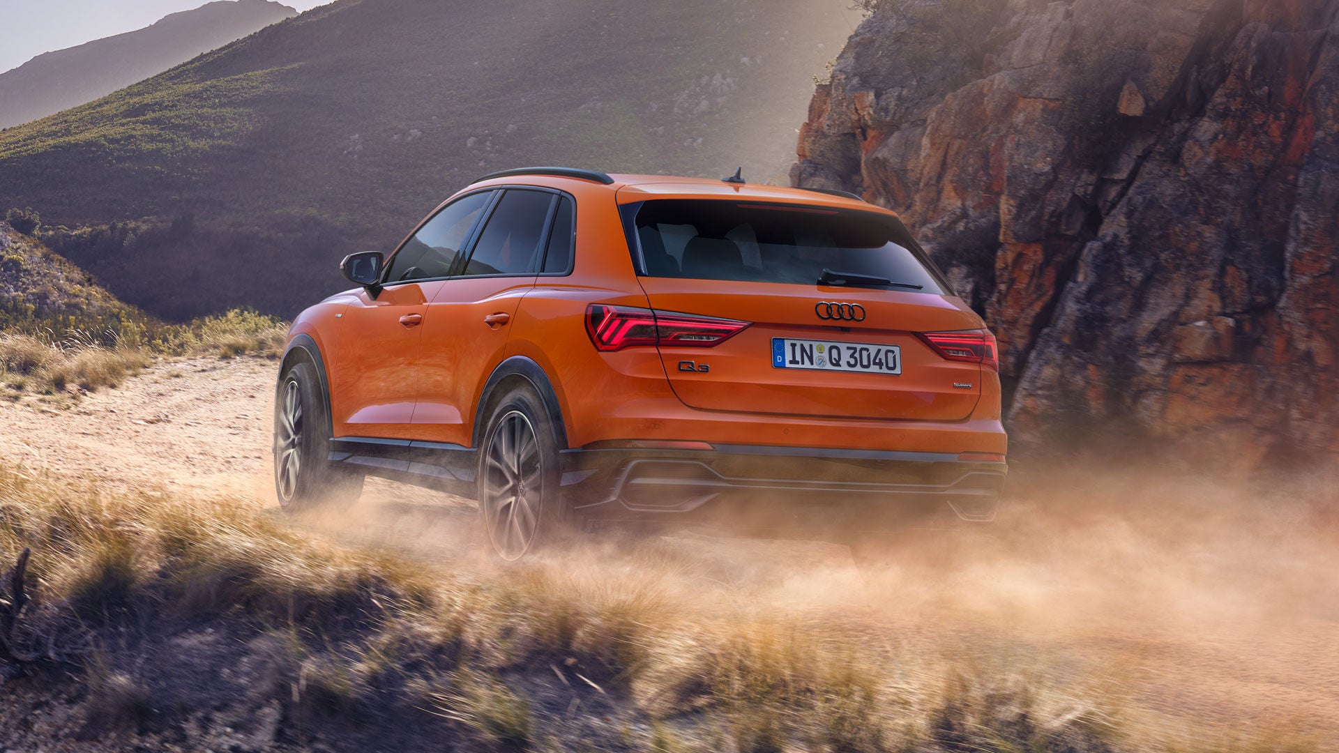 Ein orangener Audi fährt auf einer bergigen Straße, im Hintergrund Berge und Felsen leichtem Dunst.