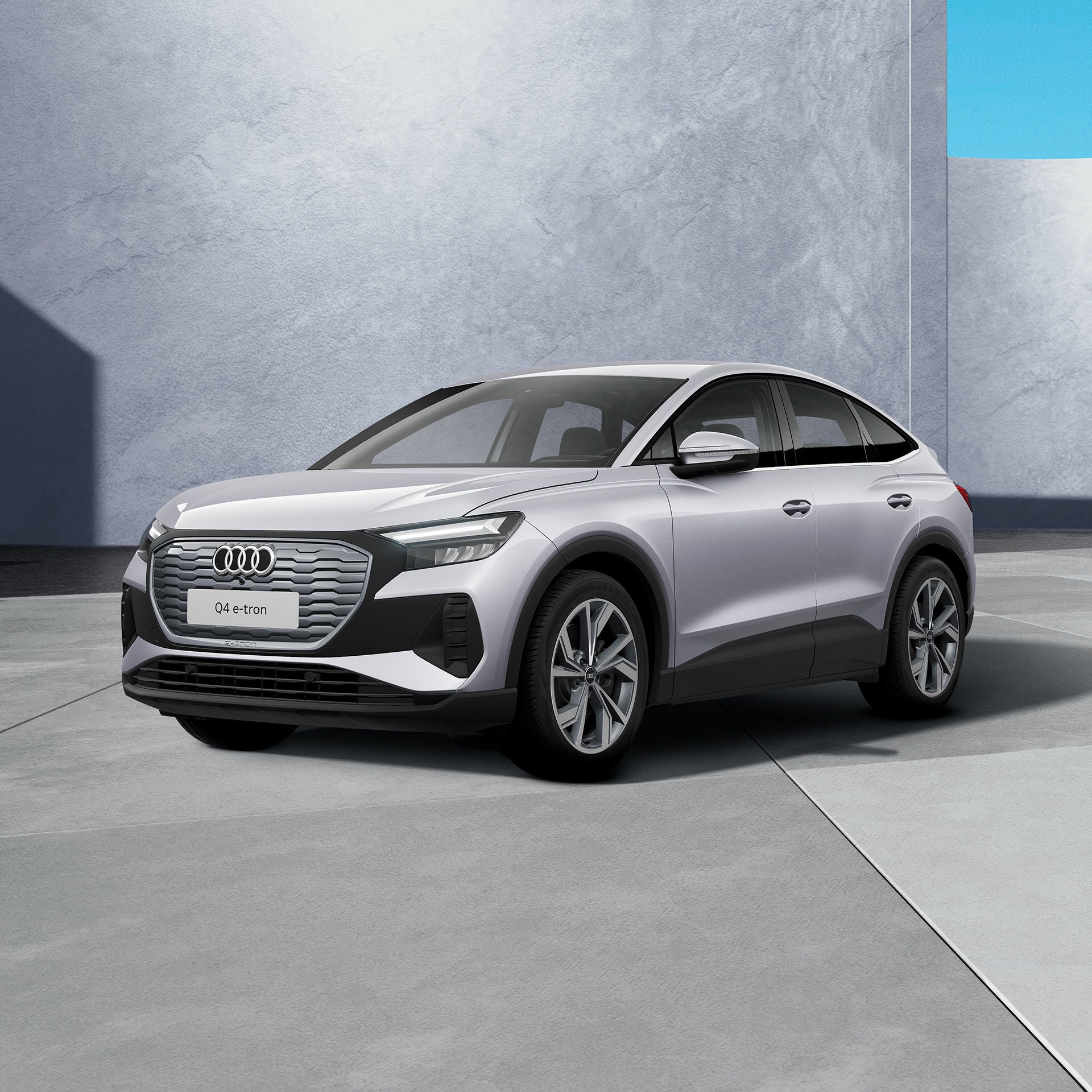 Ein grauer, moderner SUV steht in einem hellgrauen Innenraum mit großen Fenstern. Das Fahrzeug ist schräg von vorne dargestellt und wird von natürlichem Licht beleuchtet.