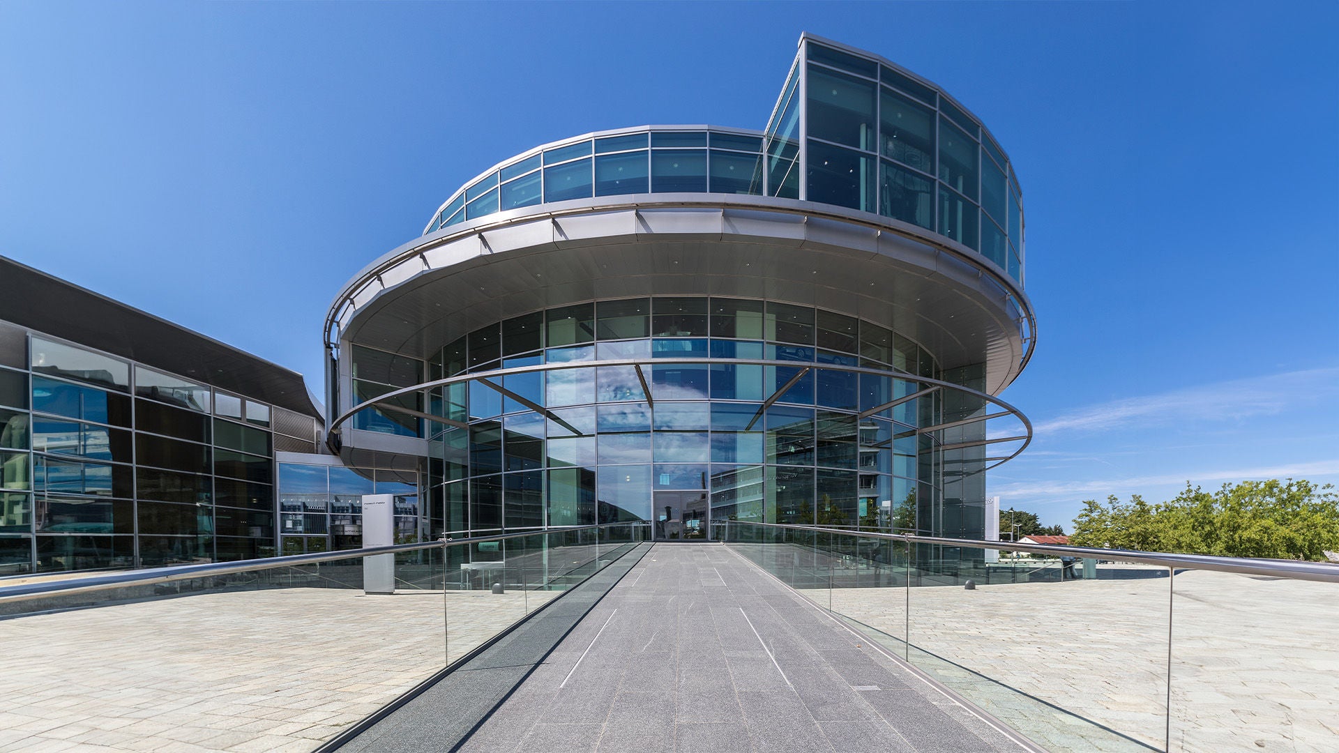 Modern round glass building with wide entrance and blue sky in the background.