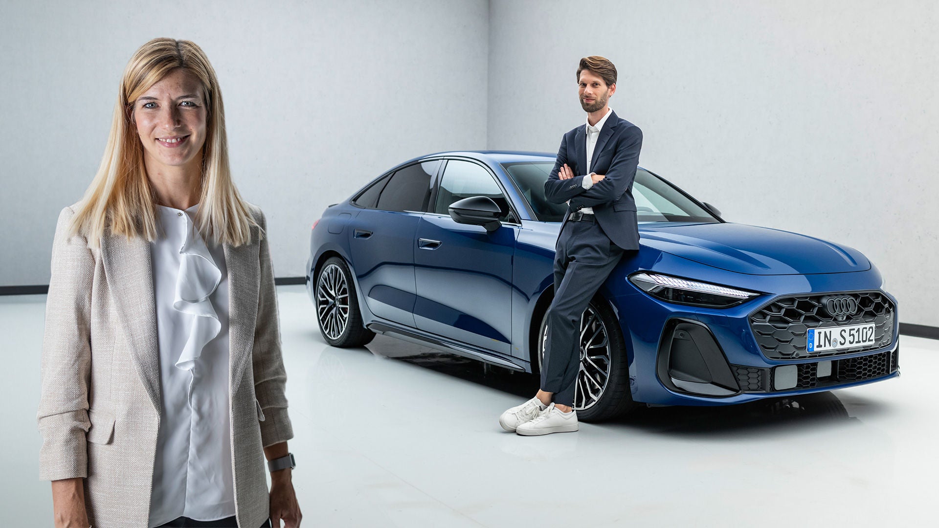 Luisa Werther stands in the foreground, Jakob Hirzel leans against a blue Audi A5 in the background