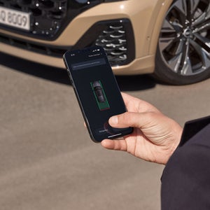 Eine männliche Hand hält ein Smartphone, auf dem Display ist ein Fahrzeug zu erkennen. Der Mann steht vor einem Q8 SUV, der im Anschnitt zu sehen ist.