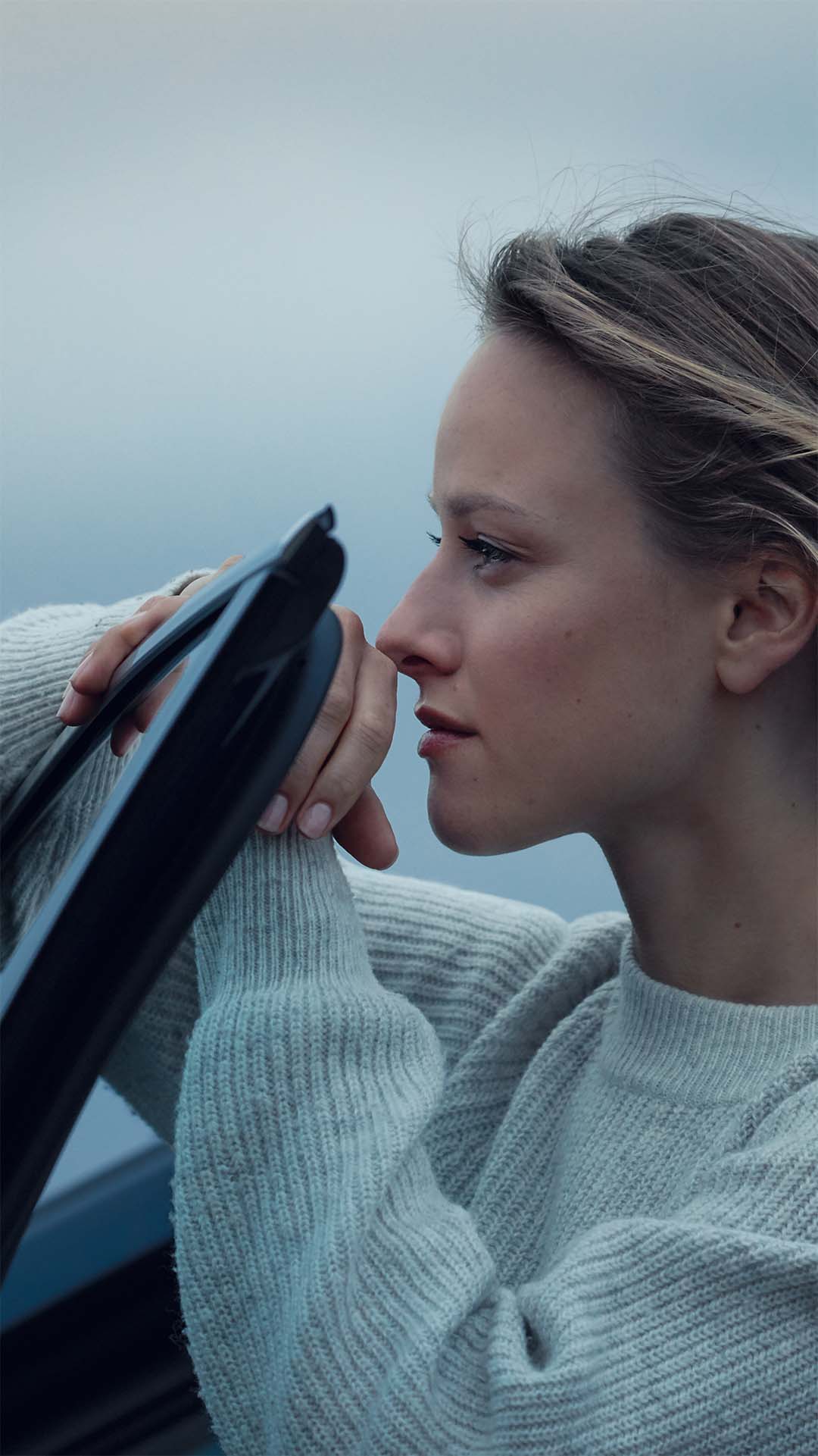 Kvinne lener seg på bildør og ser utover