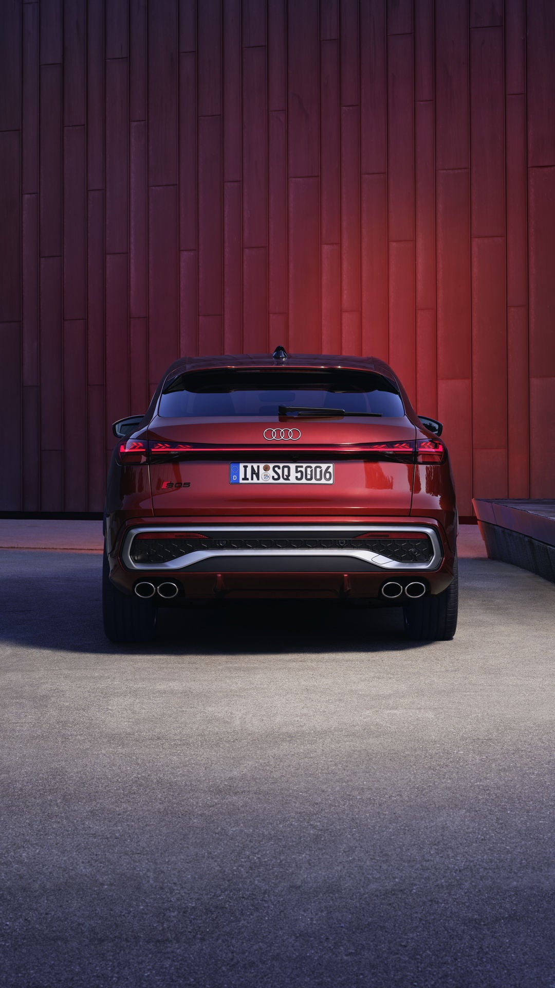 Heckprofil des roten SQ5 Sportback vor einer Gebäudefassade, die vom Fahrzeug rot angeleuchtet wird.