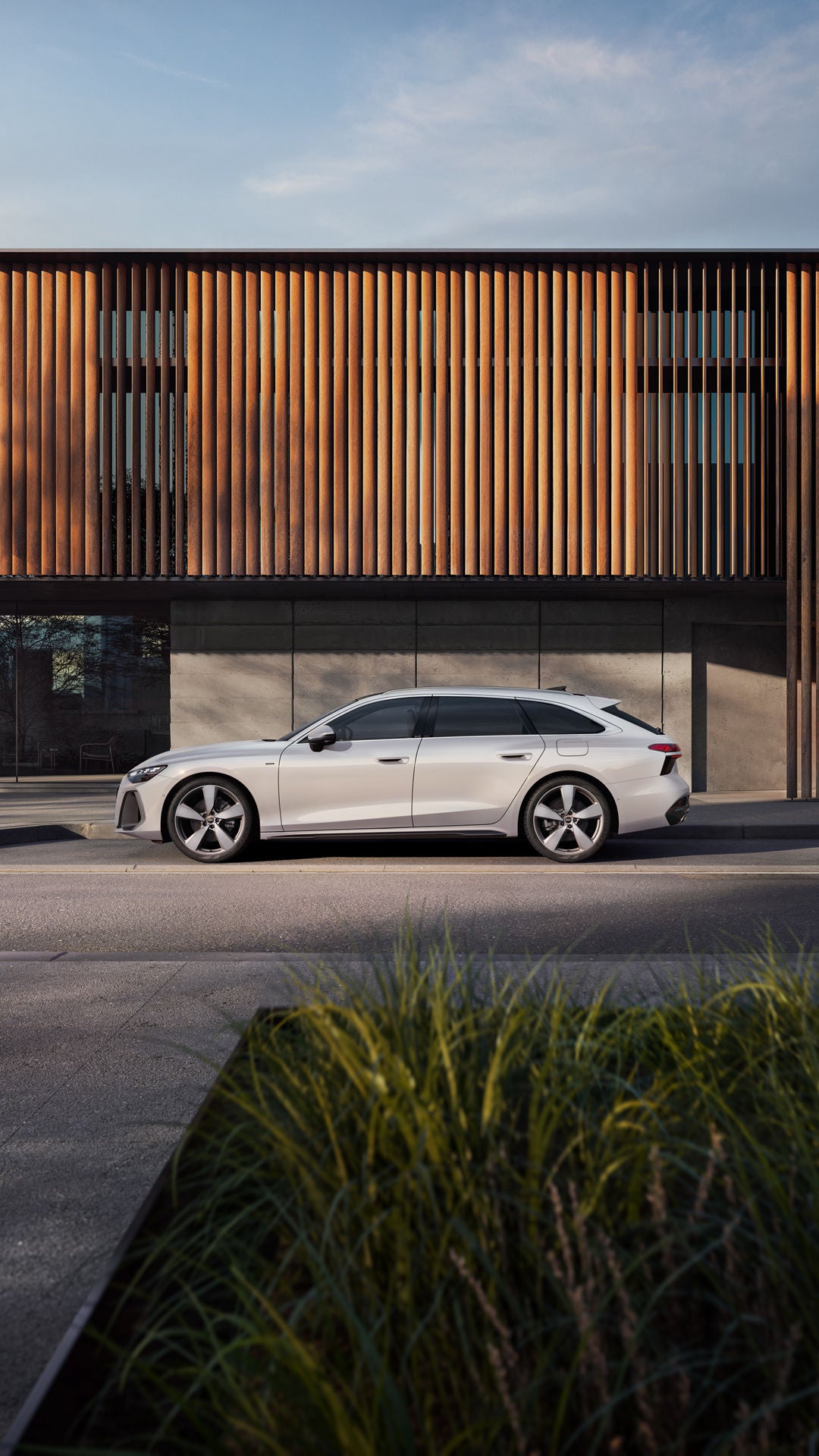 Der A6 Avant e-hybrid steht im Seitenprofil in einer Parkbucht vor der Fassade eines Gebäudes.