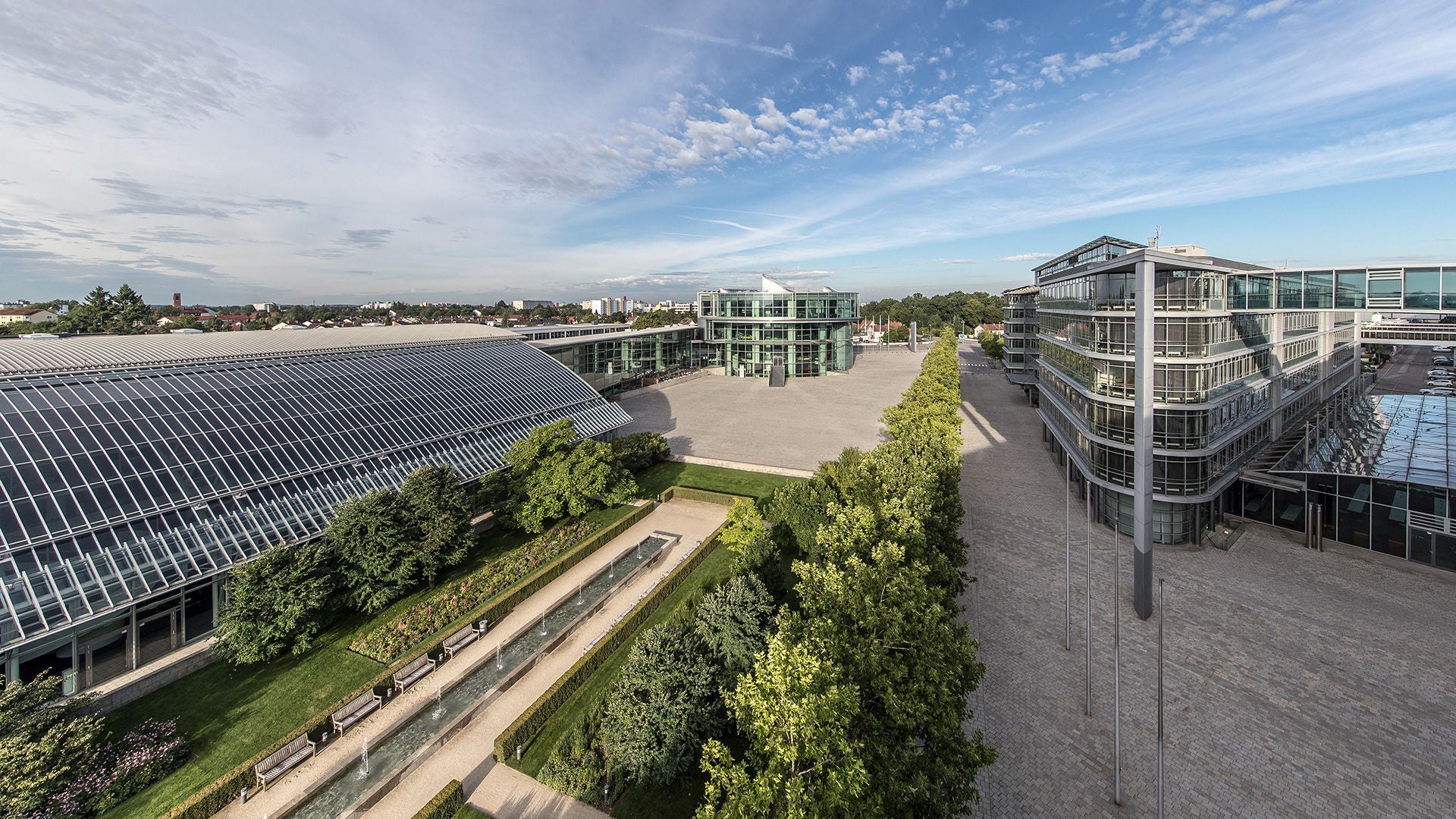 View of modern buildings with glass facades, wide forecourt and green area in daylight.