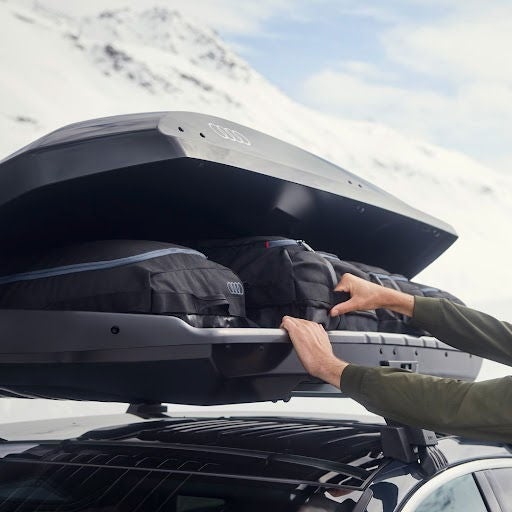 man unloading items from a roof rack with mountain range in the background 