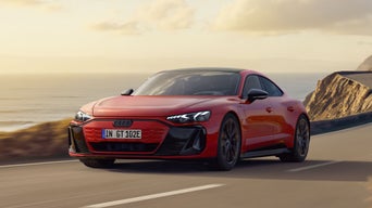 Der e-tron GT quattro fährt bei Sonnenuntergang über eine kurvige Straße entlang einer felsigen Küste.