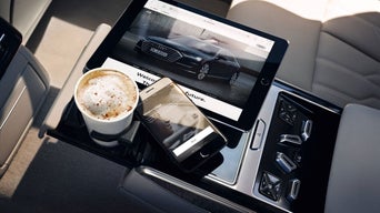 Eine Mittelkonsole im Innenraum eines Audi. Ein Smartphone und ein Tablet sind zu sehen sowie ein Kaffeebecher.