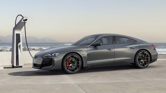 Ein grauer Audi RS e-tron GT lädt an einer Ladestation an der Küste mit Wellen und Bergen im Hintergrund.