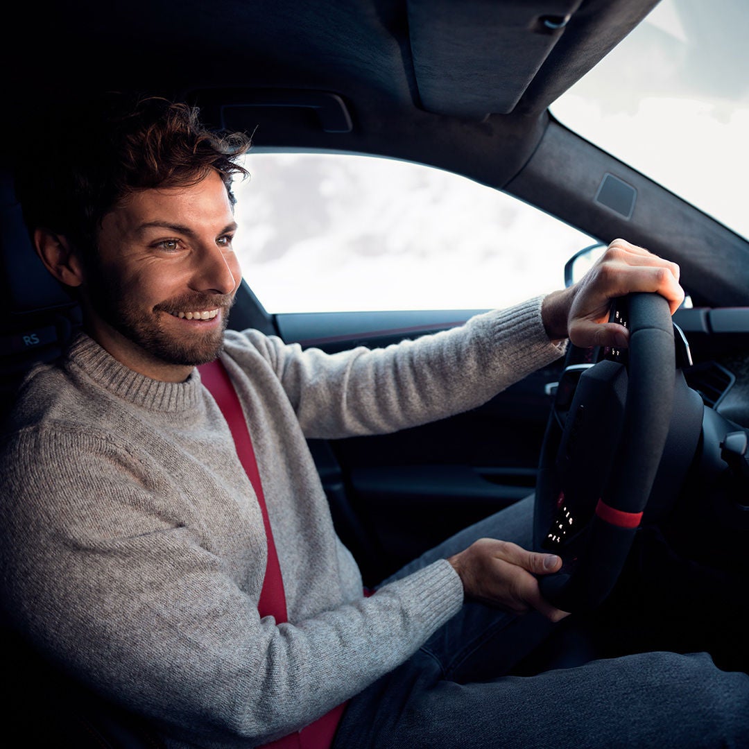 A smiling man is sitting behind the wheel of a car, looking straight ahead.