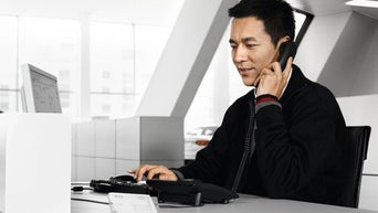 Mitarbeiter telefoniert am Schreibtisch und arbeitet gleichzeitig am Computer.