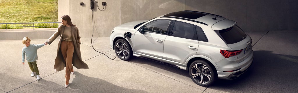 A white Audi vehicle on charge at a home with a mother and son walking away from to the left