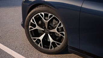 Nahaufnahme einer schwarzen Audi Felge mit silbernem Speichendesign an einem dunkelblauen Fahrzeug.