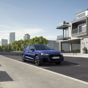 Een blauwe A1 Sportback rijdt voor een moderne woningcomplex langs.