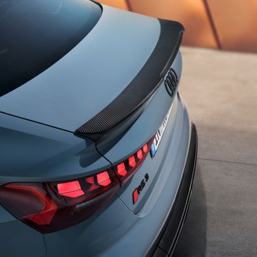 Rear view of a blue Audi RS3 Saloon with carbon fiber spoiler, showing the logo, taillights, and RS 3 badge.