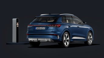 De Audi Q4 SUV e-tron, van achteren in een schuine hoek gefotografeerd tegen een donkere achtergrond, met links een laadstation.